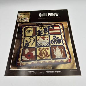 May include: A quilt pillow pattern with a patchwork design. The pillow features various squares with floral, fruit, and flag motifs. The design size is 11.5" x 11.5" (29.2 cm x 29.2 cm), and the finished pillow size is 12" x 12" (30.5 cm x 30.5 cm).