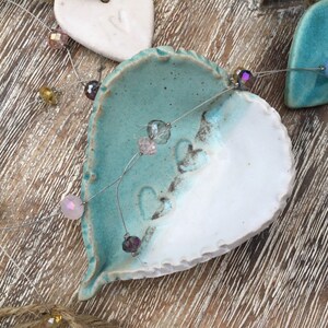 May include: A string of iridescent beads hangs between two ceramic hearts. One heart is white with a blue glaze on the top half, and the other is a solid blue.
