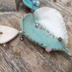 May include: A ceramic heart ornament with a white and blue glaze. The heart is decorated with a string of iridescent beads.