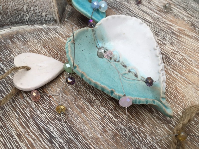 May include: A ceramic heart ornament with a white and blue glaze. The heart is decorated with a string of iridescent beads.