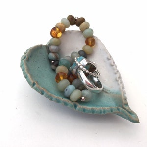 May include: A teal and white heart-shaped ceramic dish with a beaded bracelet and a silver ring inside.