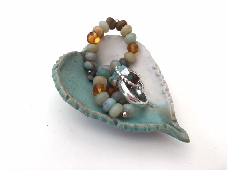 May include: A teal and white heart-shaped ceramic dish with a beaded bracelet and a silver ring inside.