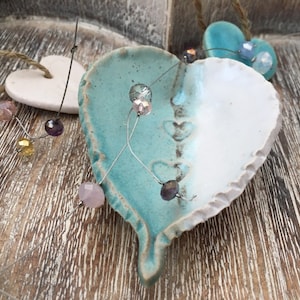May include: A white and turquoise ceramic heart ornament with a wire strung with colorful beads. The heart has a rough, textured surface and is decorated with small hearts.