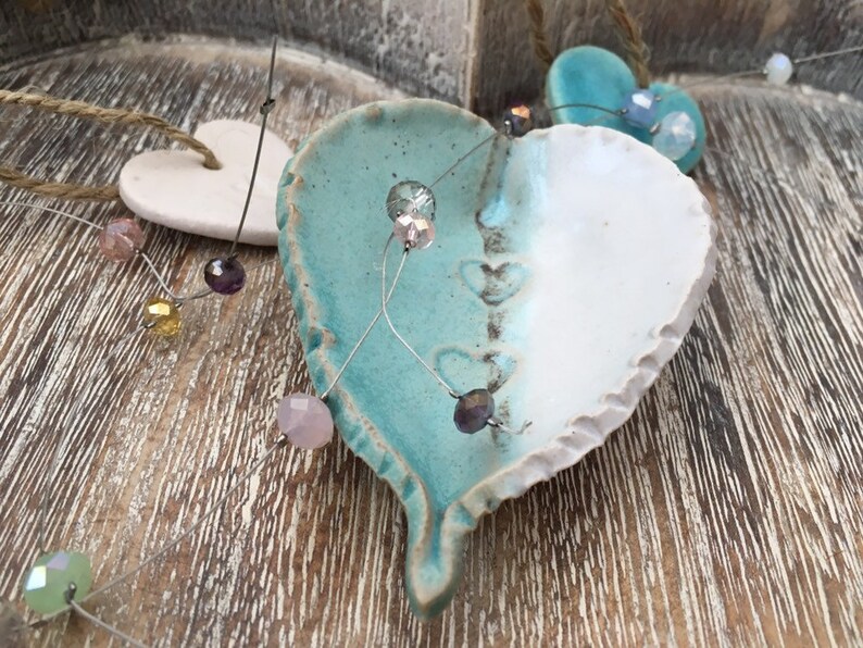May include: A white and turquoise ceramic heart ornament with a wire strung with colorful beads. The heart has a rough, textured surface and is decorated with small hearts.