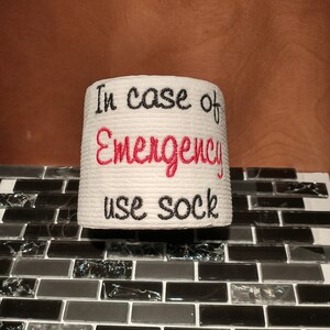 May include: White toilet paper roll with red and black embroidery that reads "In case of Emergency use sock".