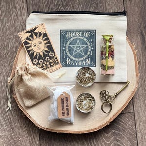 Peut inclure: Une pochette en toile blanche avec une fermeture éclair, ornée d'un pentagramme et du texte "House of Raydan". La pochette contient une carte de tarot, un petit sachet de thé à la camomille, deux bougies chauffe-plat, une petite bouteille en verre avec des herbes séchées et une clé avec un charme pentagramme.