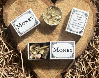 May include: Three small white boxes with the word "MONEY" printed on them. The boxes contain a key charm, a small bottle of herbs, and a white candle with dried herbs.