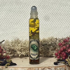Pode incluir: Uma garrafa de vidro transparente com um topo de rolamento cheio de um l&iacute;quido amarelo e ervas verdes. A garrafa tem um r&oacute;tulo que diz "Elixir de Oasis Esmeralda".