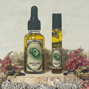 Pode incluir: Duas garrafas de vidro de elixir de o&aacute;sis esmeralda, uma em uma garrafa conta-gotas e outra em uma garrafa de rolo. Ambas as garrafas est&atilde;o cheias de um l&iacute;quido verde e t&ecirc;m um r&oacute;tulo com o texto "Elixir de o&aacute;sis esmeralda".
