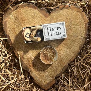 May include: A small white box with the words "Happy Home" on it, a small wooden heart with a symbol on it, and a small candle on a wooden heart-shaped surface.