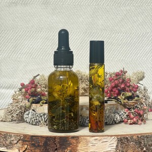 Pode incluir: Duas garrafas de vidro com tampas pretas cheias de um l&iacute;quido amarelo e ervas e flores secas. As garrafas est&atilde;o sobre uma superf&iacute;cie de madeira.