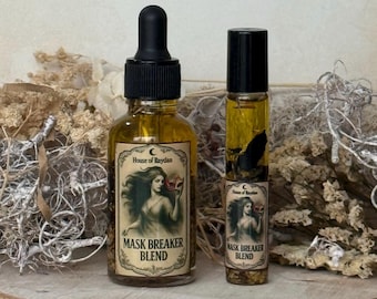 Pode incluir: Duas garrafas de vidro de óleo Mask Breaker Blend. Uma com conta-gotas, a outra com roll-on. Ambas têm rótulos com uma mulher segurando uma máscara e o texto "House of Raydan". As garrafas estão em uma superfície de madeira.