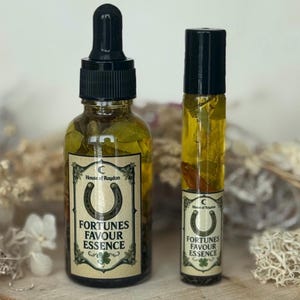 Può includere: Due bottiglie di vetro di "Fortunes Favour Essence" con tappi neri ed etichette con un ferro di cavallo e un trifoglio. La bottiglia più grande ha un contagocce ed entrambe contengono erbe visibili. Il testo "House of Raydan" è anche sull'etichetta.