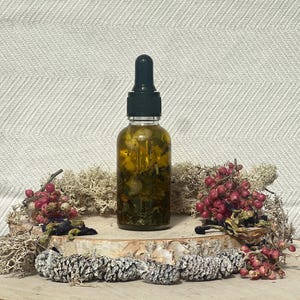 Pode incluir: Uma garrafa de vidro transparente com um conta-gotas preto cheio de um l&iacute;quido amarelo e ervas secas. A garrafa est&aacute; sobre uma superf&iacute;cie de madeira com flores e bagas secas.