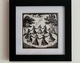 May include: A black and white illustration of a group of witches dancing in a circle in a forest. The witches are wearing pointed hats and long dresses. The illustration is framed in a black frame.