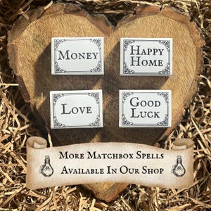 May include: Four white matchboxes with black lettering on a wooden heart-shaped surface. The matchboxes have the words "Money", "Happy Home", "Love", and "Good Luck" on them. The text "More Matchbox Spells Available In Our Shop" is on a scroll with a bottle design on each end.