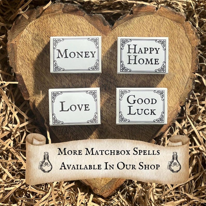 May include: Four white matchboxes with black lettering on a wooden heart-shaped surface. The matchboxes have the words "Money", "Happy Home", "Love", and "Good Luck" on them. The text "More Matchbox Spells Available In Our Shop" is on a scroll with a bottle design on each end.
