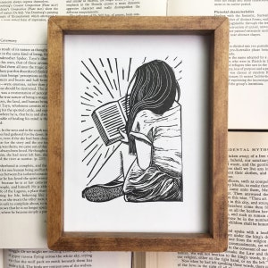 Puede incluir: Ilustraci&oacute;n en blanco y negro de una persona sentada leyendo un libro. La persona est&aacute; rodeada de un patr&oacute;n de rayos de sol radiantes.