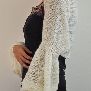 Peut inclure: Un ch&acirc;le blanc en tricot &agrave; manches longues et &agrave; la coupe ample. Le ch&acirc;le est fait d'un tissu l&eacute;ger et a&eacute;r&eacute; et pr&eacute;sente un motif d&eacute;licat et ajour&eacute;.