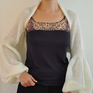 Peut inclure: Un ch&acirc;le blanc en tricot avec de longues manches bouffantes. Le ch&acirc;le est fait d'un fil doux et l&eacute;ger et a un design simple et &eacute;l&eacute;gant.