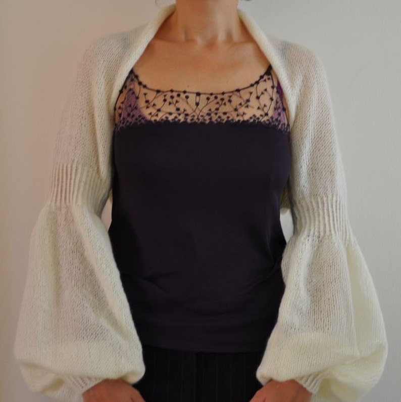 Peut inclure: Un ch&acirc;le blanc en tricot avec de longues manches bouffantes. Le ch&acirc;le est port&eacute; sur un d&eacute;bardeur noir avec une bordure en dentelle.