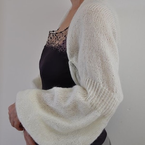 Peut inclure: Un ch&acirc;le blanc en tricot &agrave; manches longues. Le ch&acirc;le est fait d'un fil doux et l&eacute;ger et pr&eacute;sente un motif d&eacute;licat et ajour&eacute;.