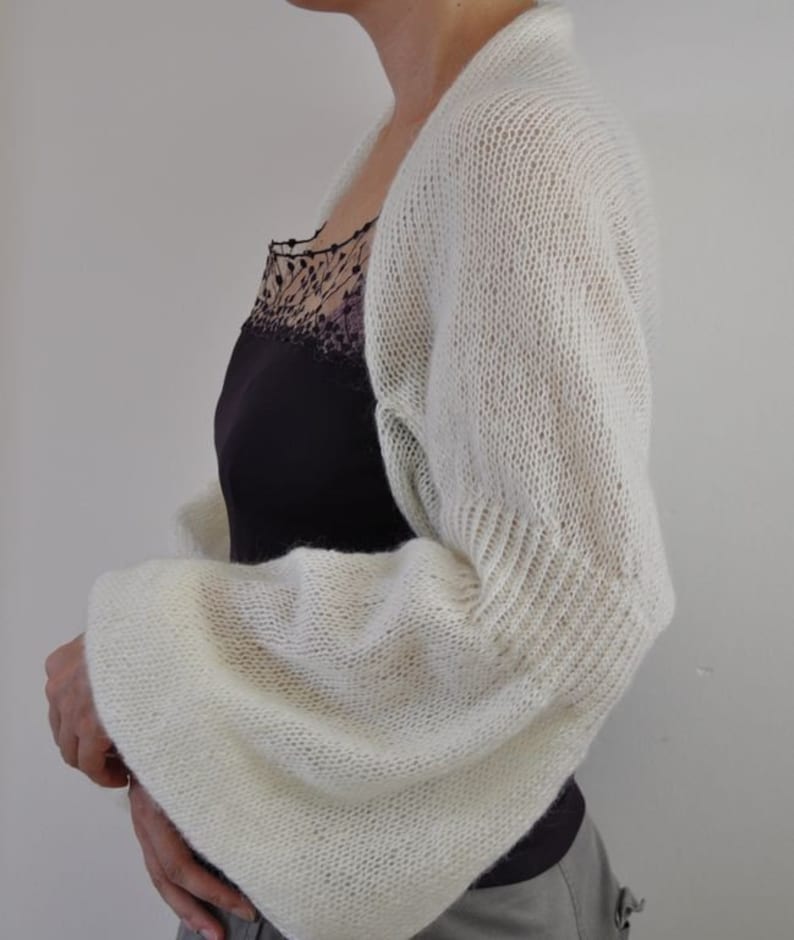 Peut inclure: Un ch&acirc;le blanc en tricot &agrave; manches longues. Le ch&acirc;le est fait d'un fil doux et l&eacute;ger et pr&eacute;sente un motif d&eacute;licat et ajour&eacute;.