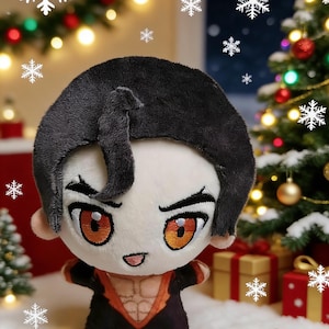 Puede incluir: Una muñeca de peluche con cabello negro y ojos anaranjados, vestida con un atuendo negro y naranja. La muñeca está colocada sobre un fondo navideño festivo con un árbol decorado, regalos y decoraciones de copos de nieve.