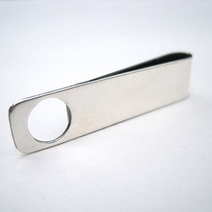 May include: A silver money clip with a circular cutout in the center.
