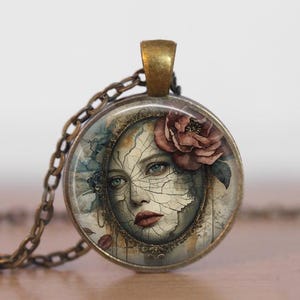 May include: A round pendant necklace with a bronze chain. The pendant features a watercolor image of a woman's face with cracked skin, blue eyes, and a red rose. The pendant has a bronze-colored frame.