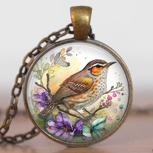 May include: A glass pendant necklace with a bronze chain features a watercolor painting of a brown and orange bird perched on a branch with purple and pink flowers. The background is a light yellow with watercolor splatters.