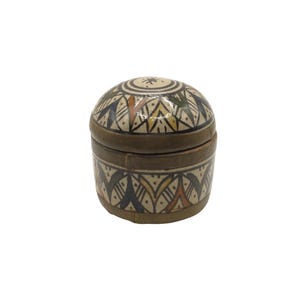 Op de afbeelding: Een kleine, ronde keramische doos met deksel met een decoratief geometrisch patroon in bruin, beige, groen en oranje. De doos heeft een donkerbruine band in het midden en op het deksel.