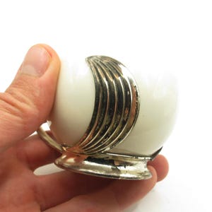 Op de afbeelding: Een witte keramische theekop met een zilverkleurige decoratieve band en voet. De kop heeft een afgeronde vorm en een klein handvat. De zilveren band heeft een geribbeld ontwerp. De kop wordt in een hand gehouden.