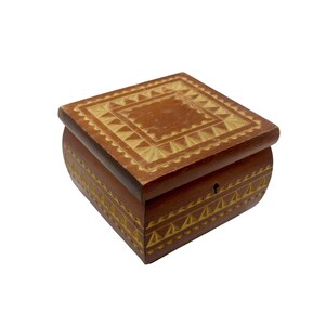 May include: A small, wooden jewelry box with a square shape and a curved base. The box is brown with intricate, carved geometric patterns in a lighter color. A keyhole is visible on the front.