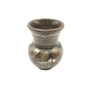 May include: A small, dark brown ceramic vase with a wide opening and a rounded body. The vase is decorated with white and brown floral patterns and a band of white scrollwork near the top. The vase is likely handmade.