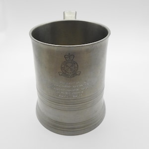 May include: A silver pewter tankard with a raised inscription and a crest featuring a crown and crossed axes. The inscription reads "Presented to The Dave Martin Ltd. in acknowledgement of their kindness and support in the successful completion of the project. January 1981."