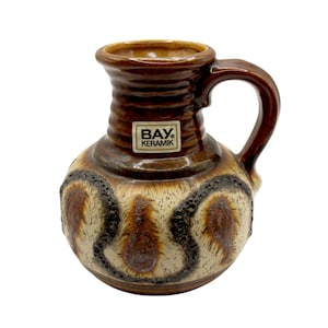 May include: A vintage ceramic pitcher with a handle, featuring a brown and tan color scheme. The pitcher has a textured design with a label that reads "BAY Keramik". The overall design is a retro style.