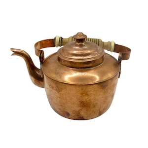 以下が含まれることがあります： 丸みを帯びたボディ、湾曲した注ぎ口、小さなノブが付いた蓋を備えた銅製のケトル。ハンドルは銅と木でできています。ケトルはおそらくヴィンテージで、使用感があります。