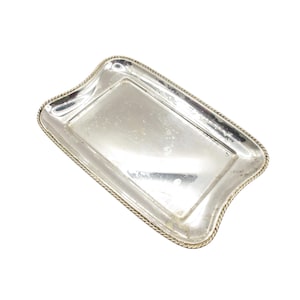 Può includere: Un vassoio rettangolare argentato con bordi curvi. Il vassoio ha un bordo a forma di corda e una superficie riflettente. Il vassoio è vuoto e sembra essere in metallo. Il vassoio è leggermente angolato.