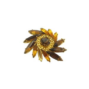 May include: A vintage brooch with a floral design. The brooch features a central, round, dark brown stone surrounded by a gold-toned setting. The petals are elongated, amber-colored stones, radiating outwards. The brooch is set against a white background.