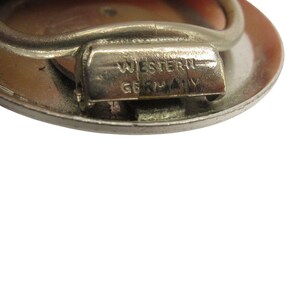 Close-up of a silver-toned metal brooch with a circular design. The brooch has a pin clasp and the text "WESTERN GERMANY" is stamped on the clasp. The brooch is set against a white background.