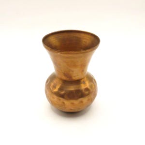 May include: A small, vintage copper vase with a bulbous base and a flared top. The vase has a hammered texture on the base and a smooth, polished finish on the top. The copper has a warm, reddish-brown hue, and the vase is set against a white background.