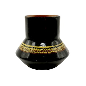 Könnte beinhalten: Eine schwarze Keramikvase mit ausgestelltem Boden und zylindrischem Oberteil. Die Vase hat ein dekoratives Band aus gelben, roten und braunen Mustern in der Mitte. Das Innere der Vase ist dunkelbraun.