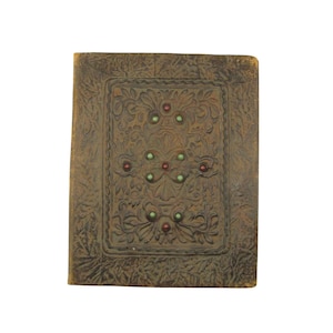 Puede incluir: Un diario rectangular de estilo antiguo con una cubierta de cuero marrón repujado. La cubierta presenta un diseño floral central con detalles rojos y verdes. Los bordes del diario también están repujados con un patrón decorativo.