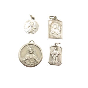 May include: Four silver-toned religious pendants of varying shapes. One round pendant depicts a figure with a halo, another rectangular pendant shows a similar figure. Two other pendants feature religious figures and text.