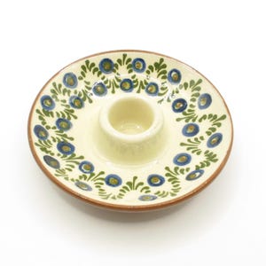 May include: A white ceramic egg cup with a blue and green floral design. The egg cup is on a small plate with the same design.