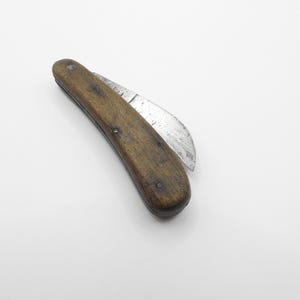 Puede incluir: Un cuchillo plegable vintage con mango de madera y hoja curva. La hoja está parcialmente abierta y el mango es de color marrón oscuro.