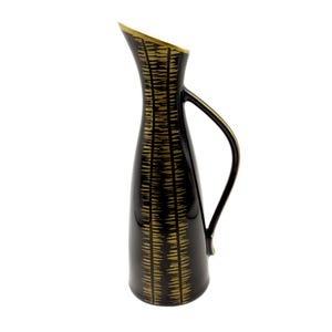 May include: A tall, black ceramic pitcher with a slender neck and a curved handle. The pitcher is decorated with a gold, textured pattern. The rim of the pitcher is also gold. This decorative pitcher is suitable for floral arrangements or as a decorative accent.