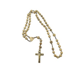 Pode incluir: Um rosário vintage com contas esculpidas de cor clara e um crucifixo de metal. As contas são conectadas por uma corrente escura, e a cruz apresenta um design detalhado. O rosário é exibido em um fundo branco.