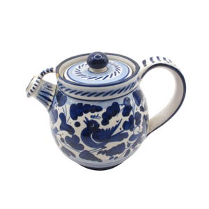 Pode incluir: Uma chaleira de cerâmica azul e branca com um design floral e de pássaros. A chaleira tem uma tampa e uma alça.